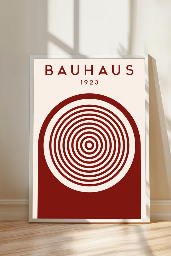 a poster with a red and white color scheme, depicting a circular design with concentric circles. The poster is titled "BAHAU 23" and is displayed on a wooden floor against a white wall.