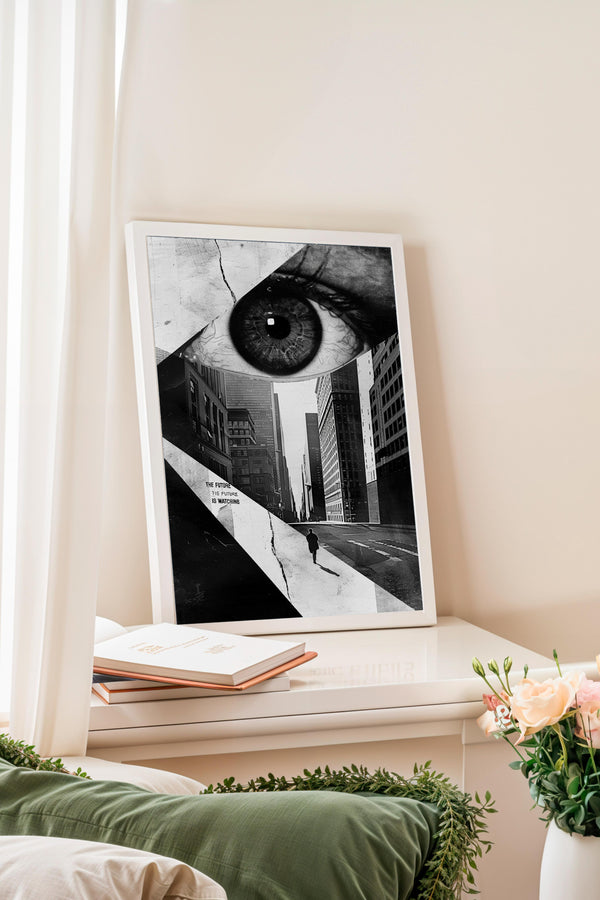a framed black and white photograph of a city street with a large eye in the center, surrounded by buildings and a lone figure walking on the sidewalk.