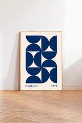 a framed poster with a geometric design in shades of blue and white, standing on a wooden floor against a white wall.