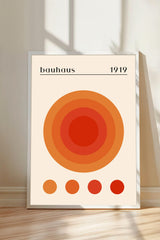 A framed poster with a large circular design in shades of orange and red, along with the text "bauhaus 1919" displayed on it.