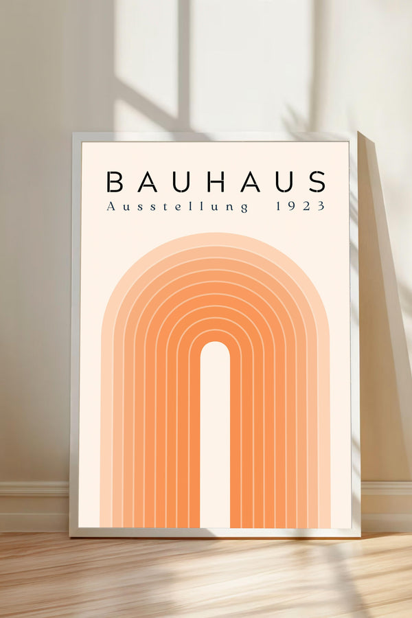a poster or artwork with the text "BAHAU" and "AUSTELLLUNG 1923" displayed prominently. The poster has a geometric design with a large arch and a series of smaller arches arranged in a repeating pattern. The poster is placed on a wooden floor, and there is a shadow cast on the wall behind it.