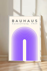 a poster or artwork with the text "BAHAU" and "AUSTELLLANG 1923" displayed prominently. The poster is framed and placed on a wooden floor, with a shadow cast on the wall behind it.