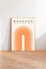 a poster of Bauhaus, a famous art school founded by Walter Gropius in 1923. The poster has a geometric design with a large arch and a series of orange lines. The text "BAHAUS" and "AUSTELLUNG 1923" is prominently displayed on the poster.
