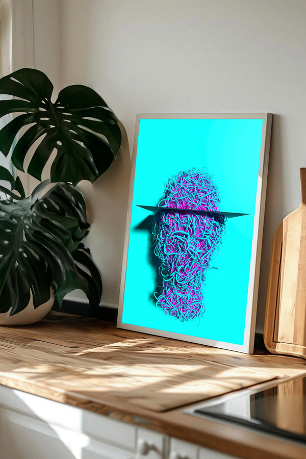 a framed artwork depicting a surreal, abstract face with a blue background and a black line cutting across it. The artwork is displayed on a wooden surface, with a potted plant and a wooden cutting board visible in the background.