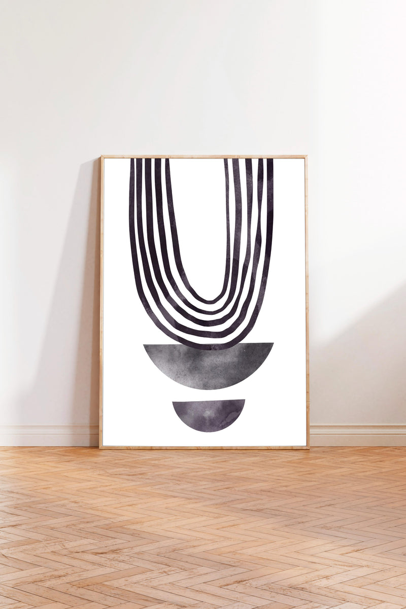a minimalist art piece with a bold, abstract design consisting of a large, curved line and two smaller, circular shapes. The art piece is displayed on a white wall in a room with a wooden floor.
