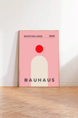 A framed poster of the Bauhaus art school from 1919, featuring a pink background with a red circle and the text "QUESSSTELLUNG 1919" and "BAUHAUS 1919" displayed prominently.