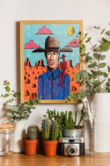 a framed painting of a cowboy with a cactus plant in a pot, surrounded by various potted plants and a vintage camera on a wooden surface.
