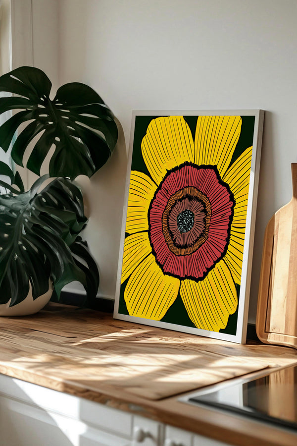 a framed artwork of a large, vibrant flower with yellow and red petals, displayed on a wooden surface.