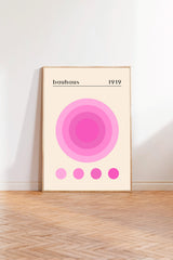 A framed poster of the Bauhaus design from 1919, featuring a large circular design with concentric circles in pink and white colors.