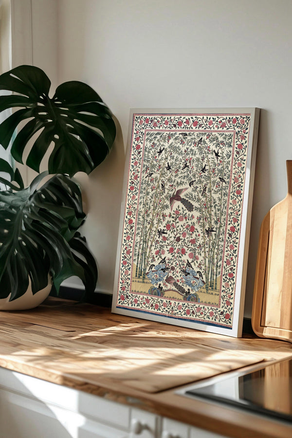 a framed picture of a bird surrounded by flowers and leaves, placed on a wooden surface next to a potted plant.