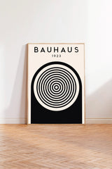 A poster of Bauhaus, a famous art school founded by Walter Gropius in 1923, is displayed on a white wall in a room with a wooden floor.