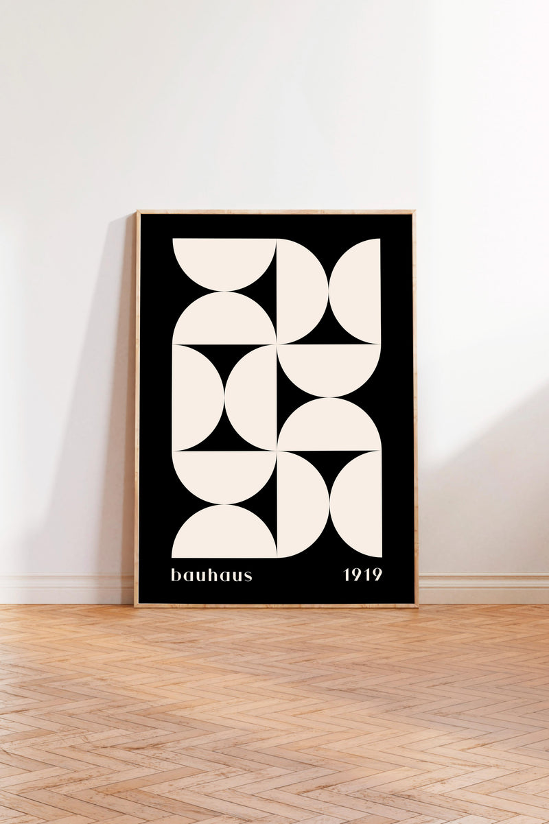a minimalist black and white geometric poster with the text "bauhaus 1919" on it, standing on a wooden floor against a white wall.