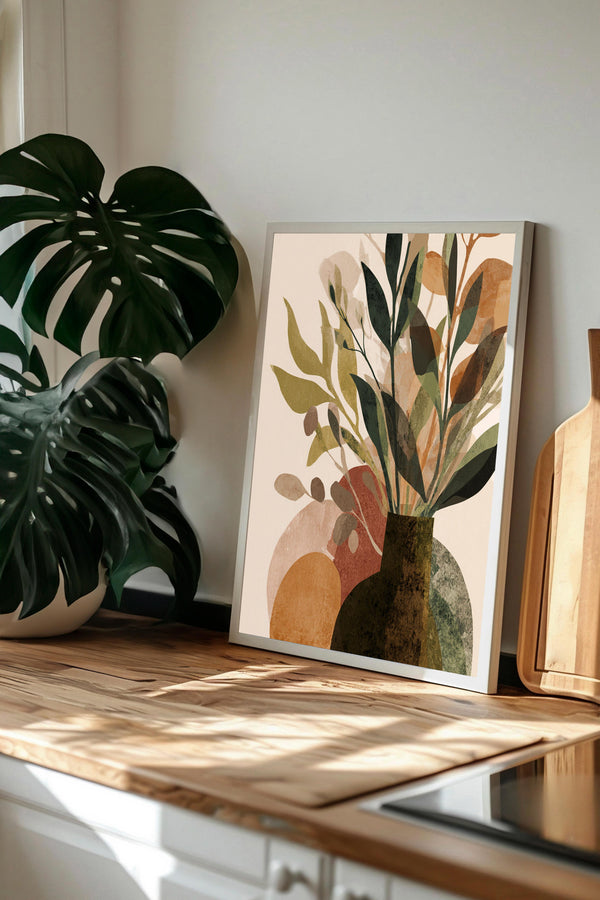 a framed print of a plant arrangement on a wooden surface, with a large monstera plant in the background.