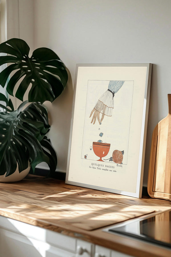 a framed illustration of a hand reaching towards a bowl of fruit, with a potted plant and a wooden cutting board in the background.
