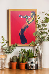 a framed painting of a person playing a trumpet, surrounded by various potted plants and a vintage camera on a wooden surface.
