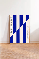 a minimalist poster with a bold blue and white color scheme, standing upright on a wooden floor against a white wall.
