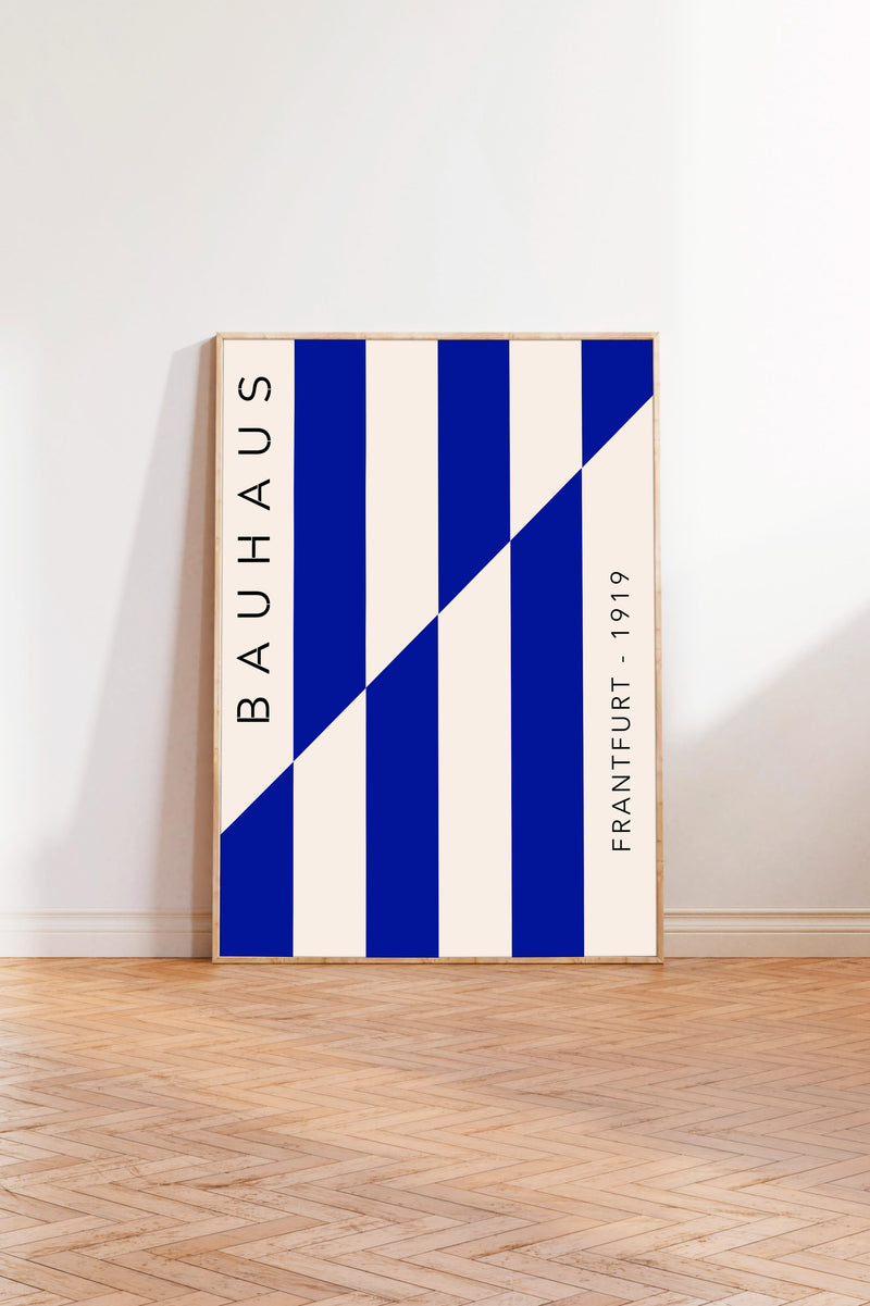 a minimalist poster with a bold blue and white color scheme, standing upright on a wooden floor against a white wall.