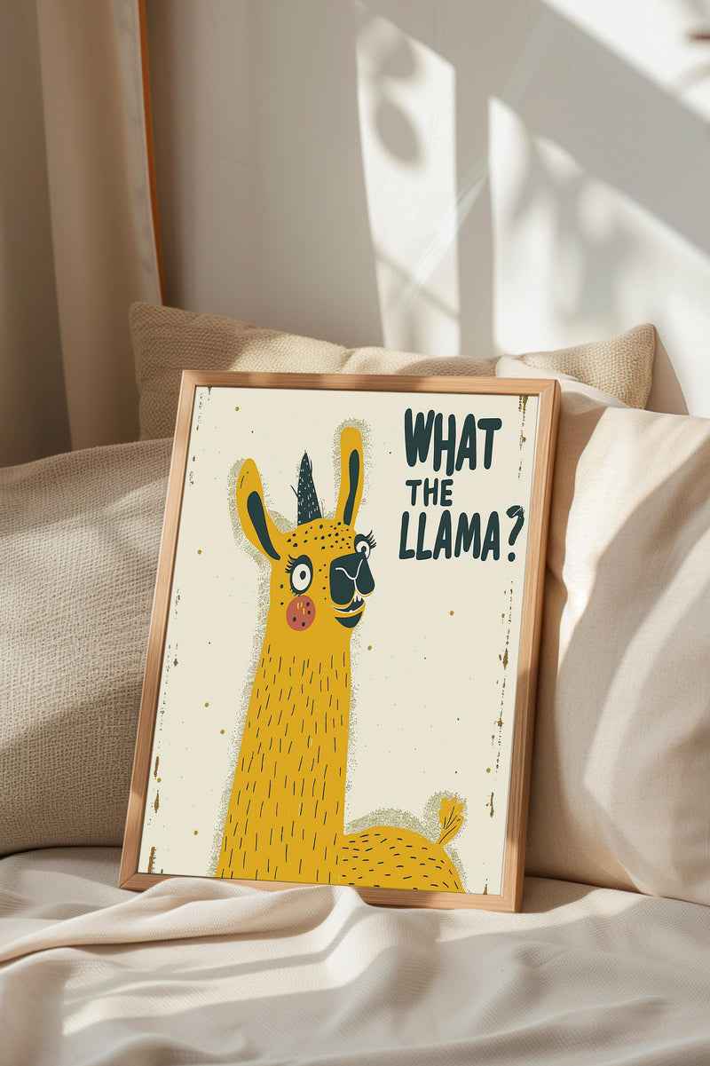 A framed illustration of a yellow llama with the text "WHAT THE LLAMA?" displayed on it, sitting on a bed with a beige pillow.